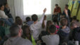 Photo avec des enfants assis de dos devant l'écran d'un vidéo projecteur. Quelques enfants lèvent la main.