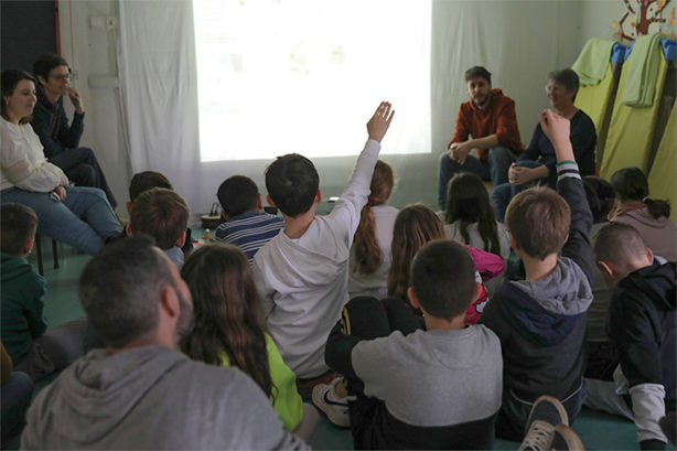 Photo avec des enfants assis de dos devant l'écran d'un vidéo projecteur. Quelques enfants lèvent la main.