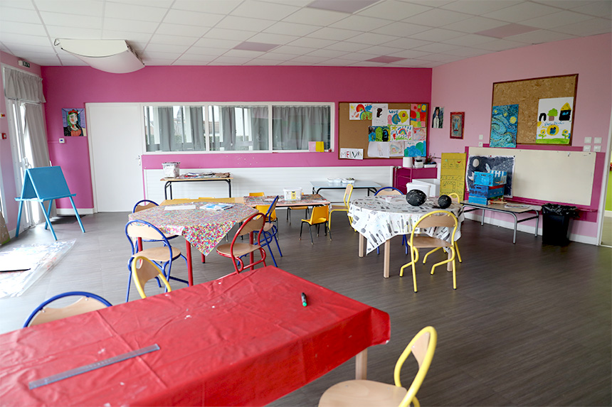 Photo de la salle créative de l'accueil de loisirs avec différentes tables et des peintures accrochées au mur