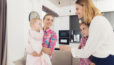 Photo de 2 femmes souriantes aux côtés de 2 enfants, dans un salon avec en arrière-plan une cuisine