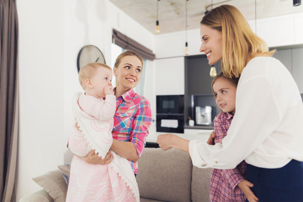 Photo de 2 femmes souriantes aux côtés de 2 enfants, dans un salon avec en arrière-plan une cuisine